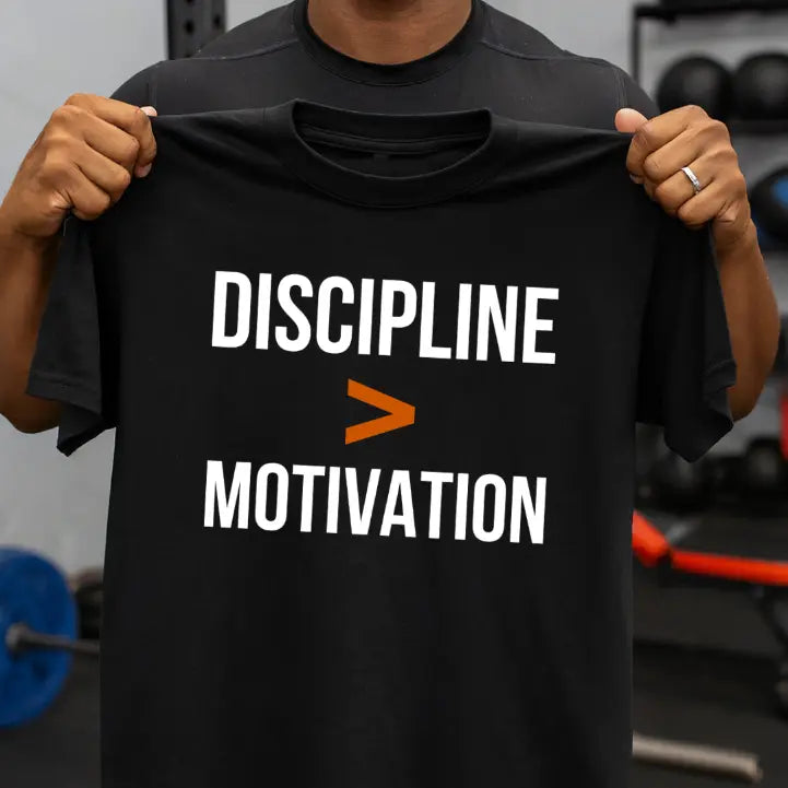 Person holding a black t-shirt with 'Discipline > Motivation' text in a gym setting