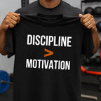 Person holding a black t-shirt with 'Discipline > Motivation' text in a gym setting